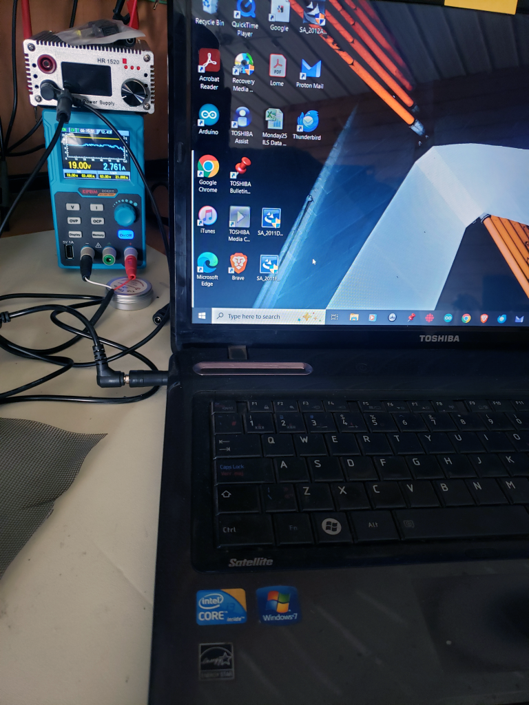 Repaired & Booting The Toshiba Satellite is now running — booting into Windows. It's being powered by a bench power supply set to 19.00V / 2.761A, which is the standard DC input for Toshiba laptops. This confirms the DC jack repair was successful.