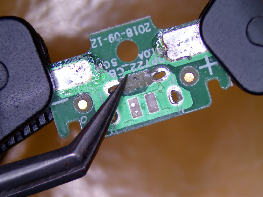 USB Micro Charging Port / Trace Repair (Close-up) A small green PCB. Tweezers show torn pad/trace damage is evident — this is classic micro-USB port tear-out damage.